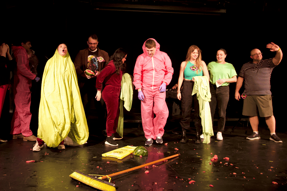 The Nova Show main cast, in various costumes, prepare to take a bow on stage covered in smashed watermelon.
